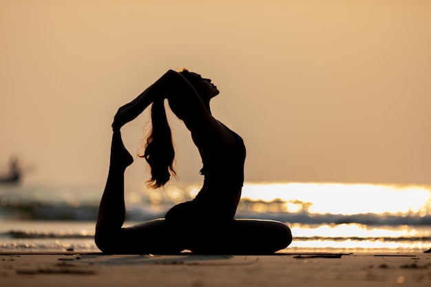 woman wearing black sportswear practicing yoga pose on the beach