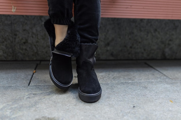 A woman wearing black suede boots sits on a bench.