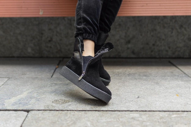 A woman wearing black suede sneakers is shown on a bench.