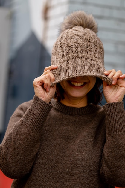 A woman wearing a brown sweater and a brown sweater holds her face up to her face and smiles.