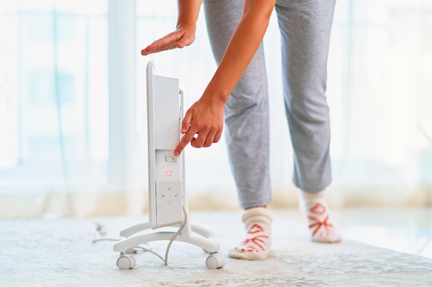 Woman wearing cozy soft knitted socks warming with electric portable heater at home