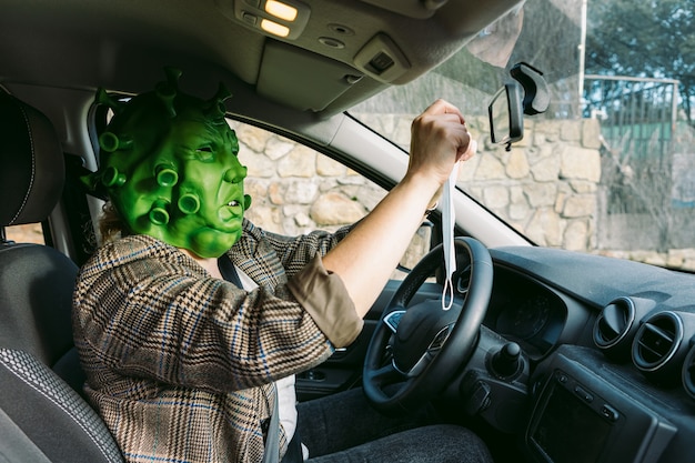 Woman wearing disguise - coronavirus covid-19 mask in the car hanging the protective mask in the clearance mirror