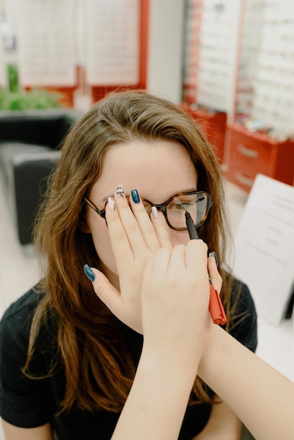 A woman wearing glasses is covering her eyes doctor with a red box behind her