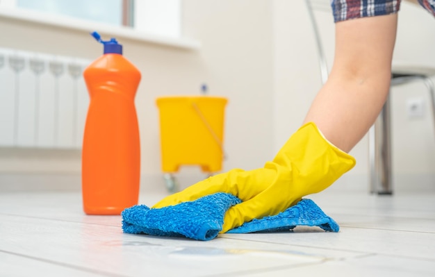 Woman wearing gloves cleaning floor cleaning and care product for laminate and flooring female hands in yellow gloves wipe wooden floor with blue microfiber cloth