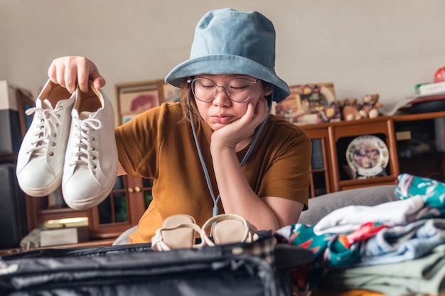 A woman wearing a hat hesitates to choose sneakers to make her choice to get away on vacation.