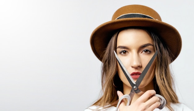 A woman wearing a hat looking through scissors hight quality