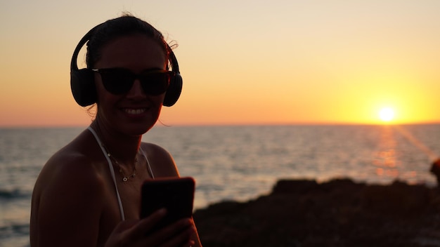 Photo a woman wearing headphones is listening to music on her phone