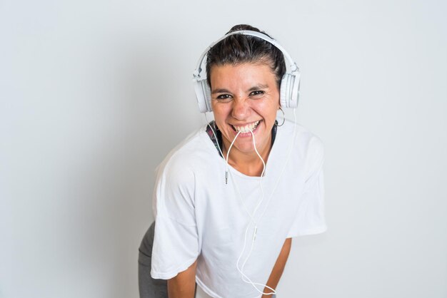 A woman wearing headphones is smiling and wearing a white t - shirt.