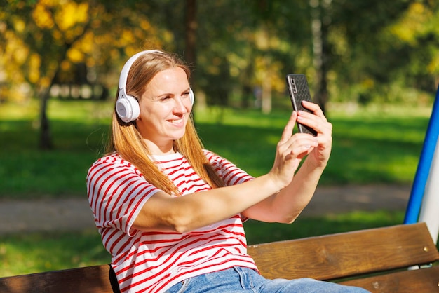 A woman wearing headphones listening to music while sitting on a bench