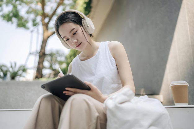 a woman wearing headphones sits on a bench and reads a book