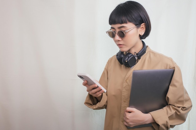 Woman wearing headphones using the phone and holding laptop computer