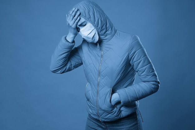 Woman wearing hood in a protective face mask and coat over blue background model girl in medical