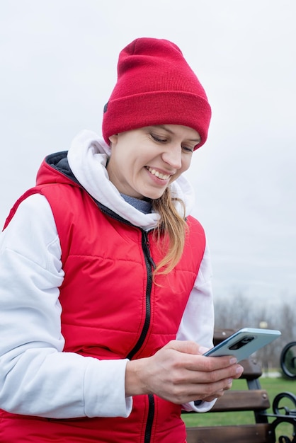 Woman wearing knee brace or orthosis after leg surgery sitting in the park using smartphone