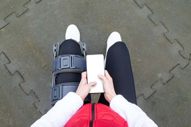 Woman wearing knee brace or orthosis after leg surgery working out in the park