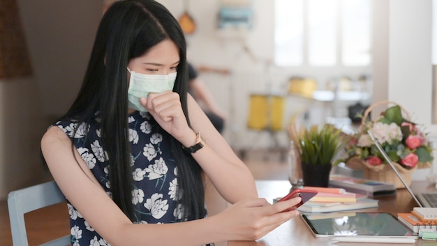 Woman wearing a mask covering her mouth coughing and using a smartphone, Medical concept, Online learning, Working from home.