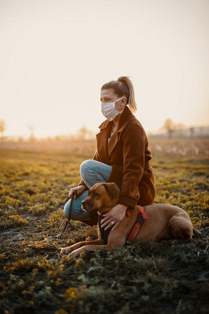 Woman wearing a mask is walking alone with a dog outdoors because of the corona quarantine