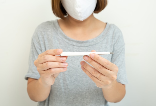 Woman wearing mask for protect Coronavirus look at Thermometer on white. Air pollution,environmental concept.

