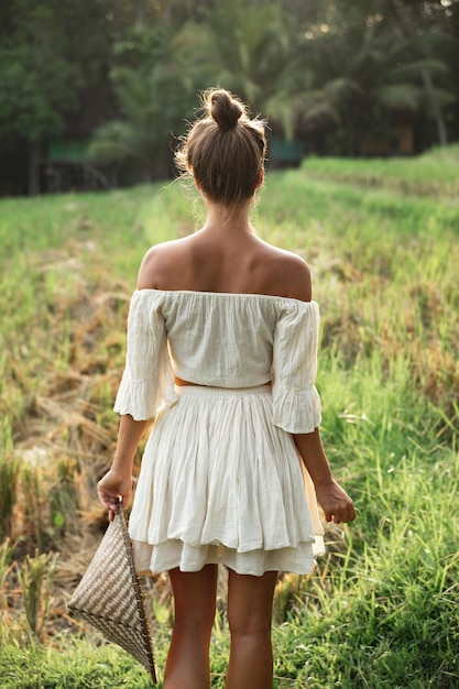 Woman wearing natural clothes holding Asian conical hat in the rice field during sunset