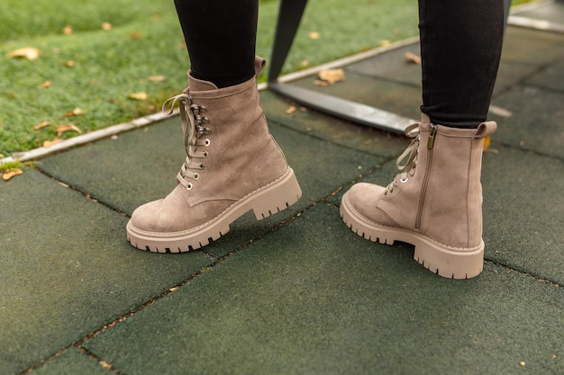 A woman wearing a pair of tan boots stands on a green carpet.