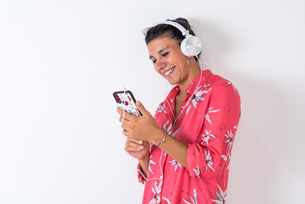 A woman wearing a pink floral dress is listening to music on her phone.