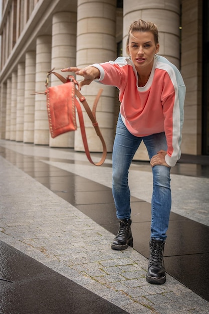 A woman wearing a pink sweater and blue jeans holds bag