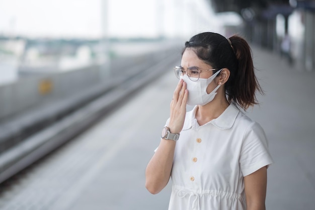 Woman wearing Protective face mask prevention coronavirus and PM 2.5 pollution during waiting train. public transportation. safety under covid-19 pandemic and dust