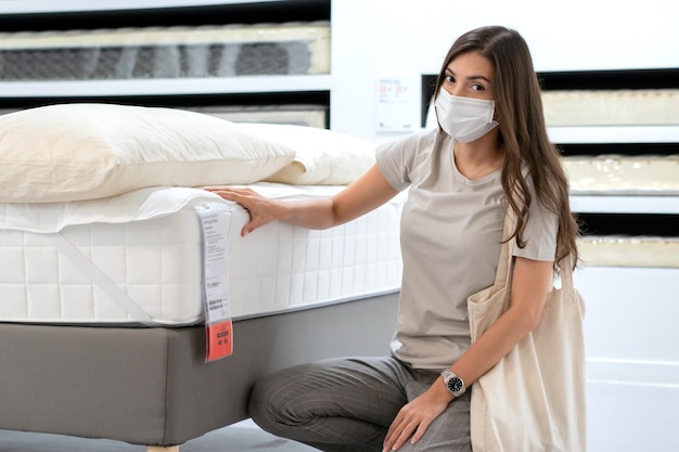 Woman wearing protective mask selecting bed mattress for moving home