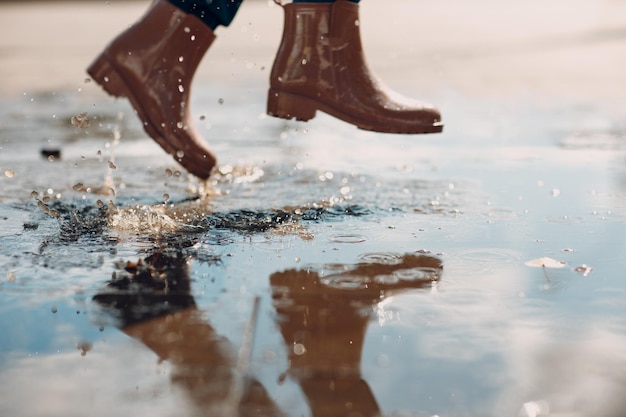 Woman wearing rain rubber boots walking running and jumping into puddle with water splash and drops