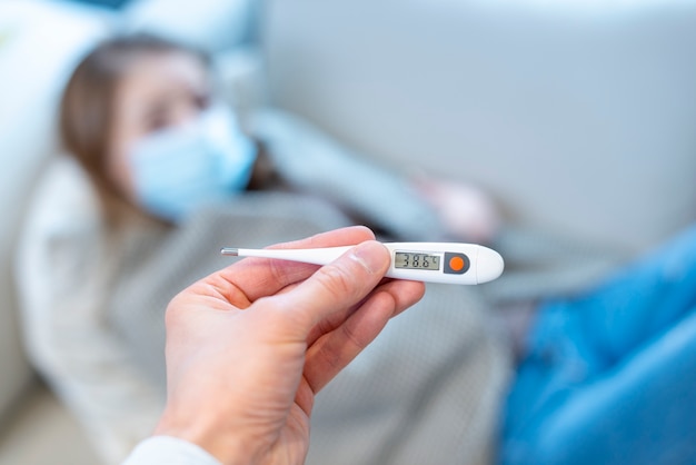 Woman wearing surgical face mask and thermometer