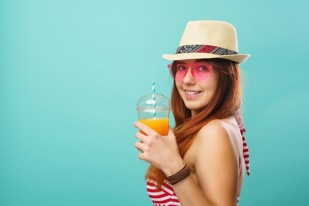 Woman wearing swimsuit and hat drinks fruit juice from a cup