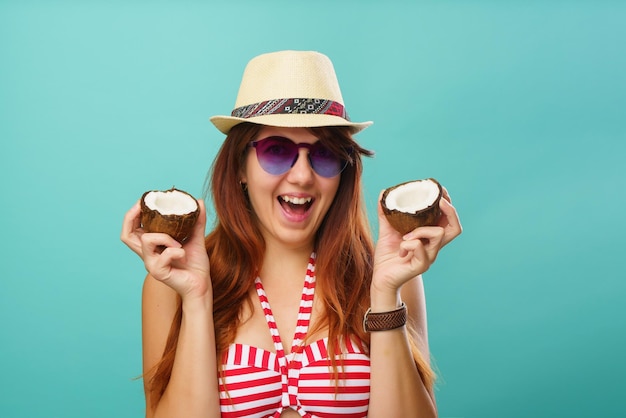 Woman wearing swimsuit and straw hat holding two part of coconaut