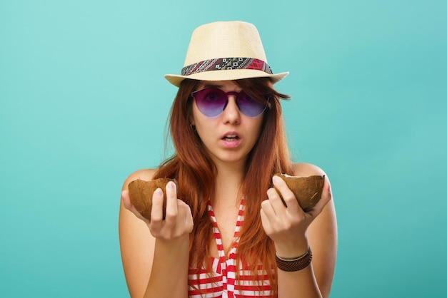 Woman wearing swimsuit and straw hat holding two part of coconaut