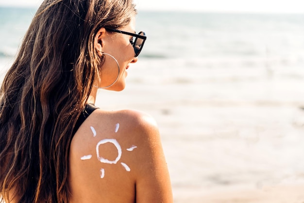 Woman wearing two piece bikini applying suncream with sun drawn on back and holding sunscreen lotion on the tropical beachYoung girl with sun block skin protectionSummer vacations