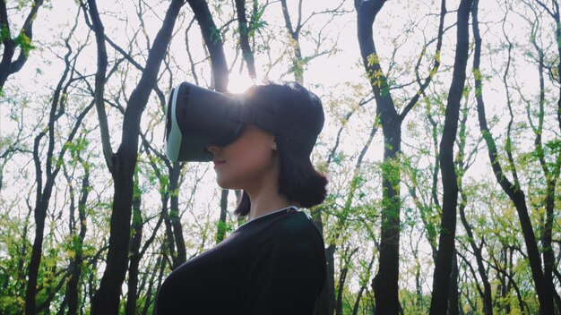 Photo woman wearing virtual reality simulator while standing on field at forest