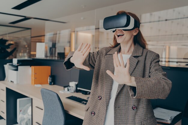 Woman wearing VR headset having fun in virtual reality game while standing in office