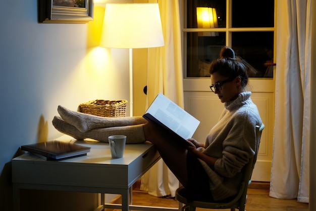 Woman wearing a warm woolen sweater is reading book