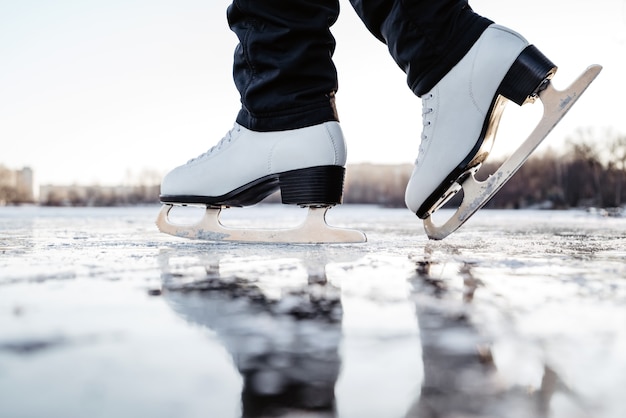 Woman wearing white fugure skates stands on ice. Winter outdoor sport activities