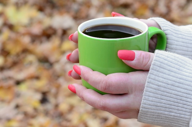 Woman wearing white sweater holding a green coffee cup