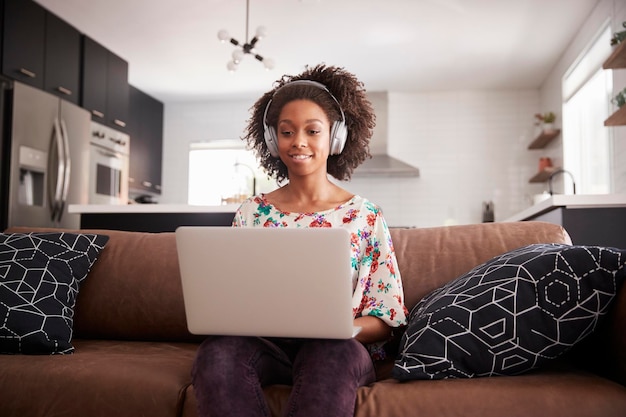 Woman Wearing Wireless Headphones Sitting On Sofa At Home Using Laptop