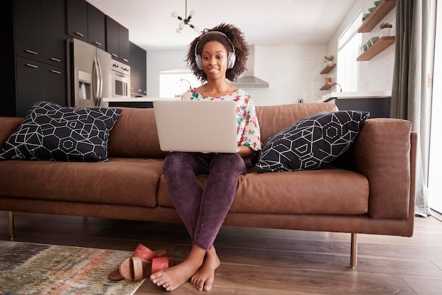 Woman Wearing Wireless Headphones Sitting On Sofa At Home Using Laptop