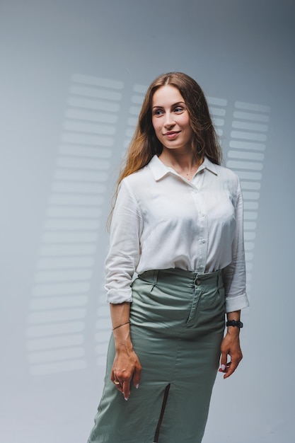 A woman wears a white blouse and skirt on a gray background emotions on a woman's face Elegant look positive woman Model in casual clothes Summer spring or autumn street look