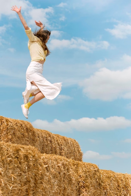 Woman while jumping on big haystack Girl has fun and jumps in the hay on blue background Summer vacation