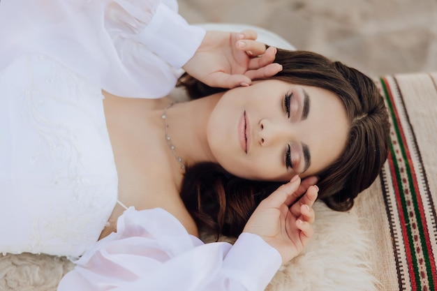 A woman in a white airy dress lies on the floor with her eyes closed