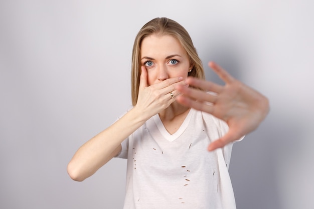 Woman on a white background closes her mouth with her hand against violence