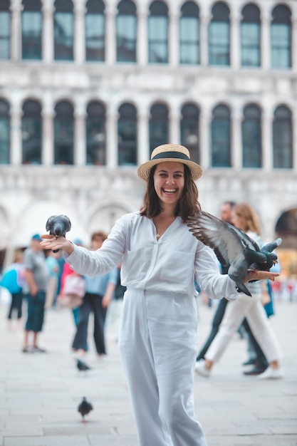 Woman in white clothes with straw hat having fun with pigeons at venice city square