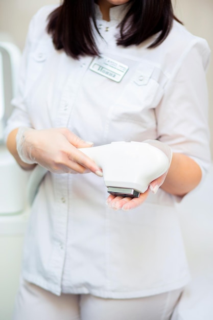 A woman in a white coat holds a laser hair removal machine in her hands