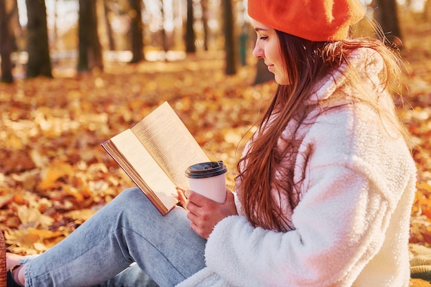 Woman in white coat is sitting in the autumn park