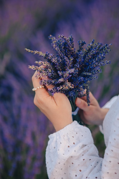 Woman in white dress holding bouquet of lavender flowers close up