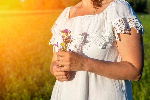 Woman in a white dress holds a bouquet of wildflowers in her hands