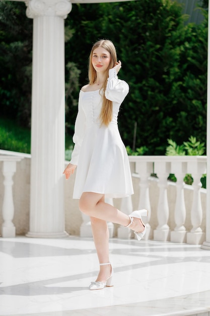 A woman in a white dress poses for a photo in front of a white pillar